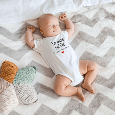 Un bébé est allongé sur le dos et il porte un barboteuse blanche tel père tel fils
