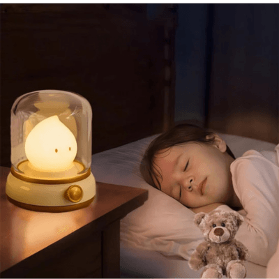 une petite fille dort éclairée par une BEBE VEILLEUSE FLAMME - Lanterne Magique™ à coté d'elle est posé un petit ours en peluche
