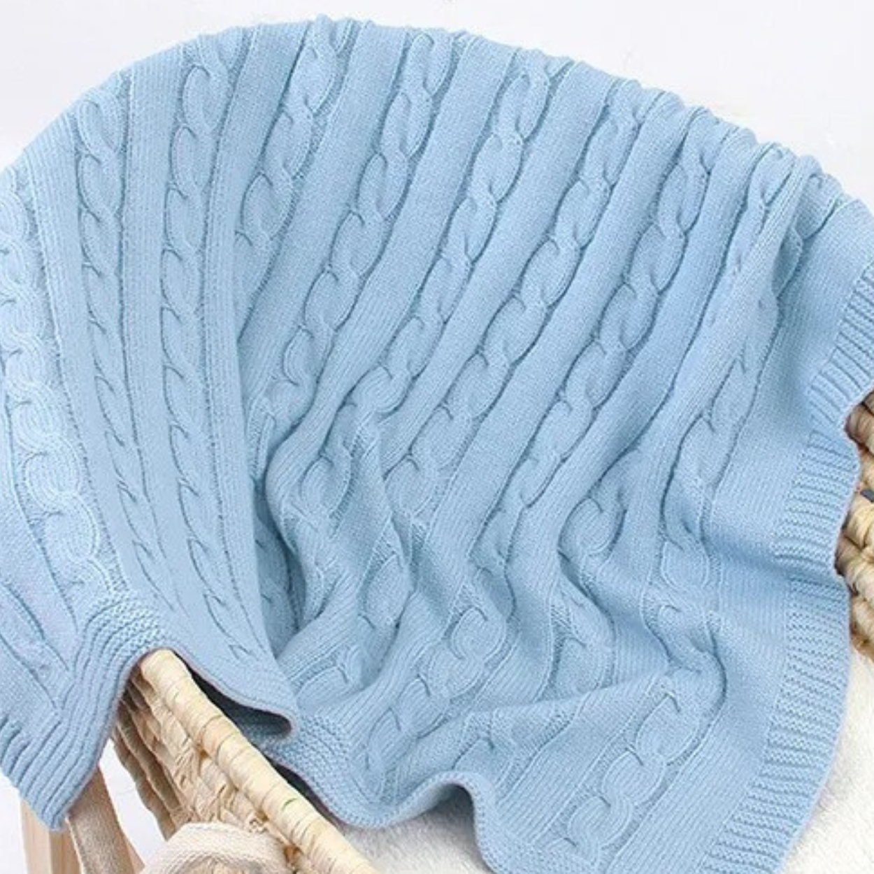 Gros plan sur la COUVERTURE BEBE TRICOT│Plumy™ bleue posée sur un couffin