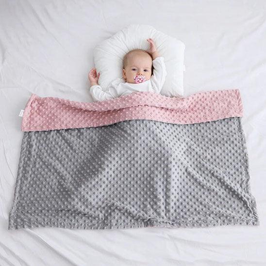 Un bébé allongé sur le dos et recouvert de la COUVERTURE BEBE REVERSIBLE - DouceBulle™rose et gris