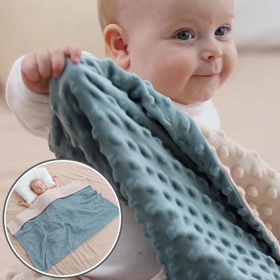 Un bébé tient à la main un coin de la COUVERTURE BEBE REVERSIBLE - DouceBulle™ en gros plan