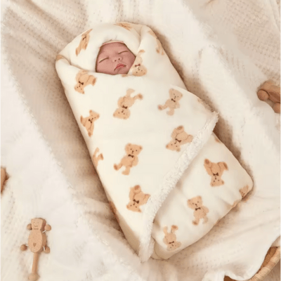 Un bébé allongé dans un couffin emmailloté dans la Couverture Bébé Animaux - Câlinou™