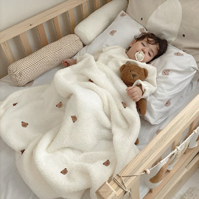 Bébé endormi dans un berceau, emmitouflé dans une Couverture Bébé Tête d'Ourson│DouDodo™ultra-douce beige.