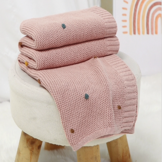Gros plan sur la Couverture Bébé Tricot Coton│DouceMaille™ - Rose posée sur un tabouret