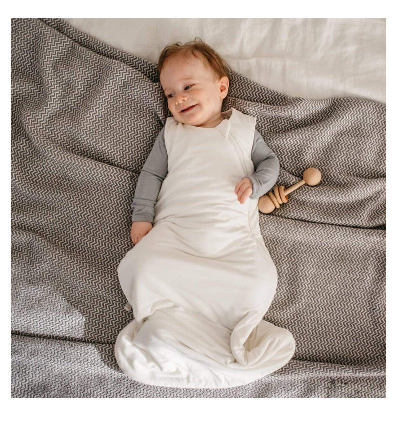 Bébé endormi sur un drap blanc, vêtu d’une gigoteuse été blanche DouxRefuge™ en bambou, les bras détendus – confort, légèreté et sécurité pendant les nuits estivales.