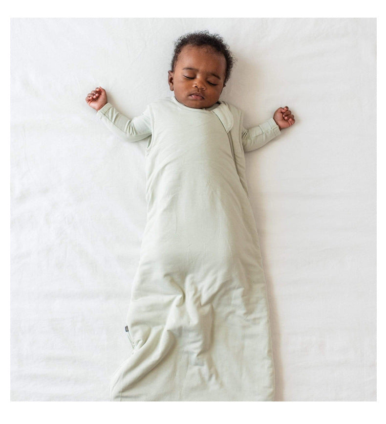 Bébé endormi sur un drap blanc, habillé d’une gigoteuse été DouxRefuge™ en bambou vert sauge, les bras détendus – douceur, sécurité et fraîcheur naturelle pour les nuits chaudes.