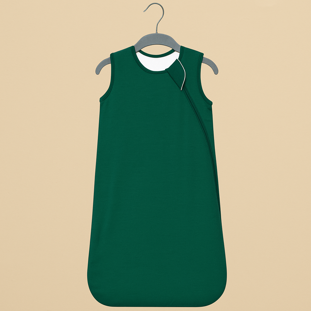 Gigoteuse Printemps et Automne vert foncé suspendue sur cintre en bois, présentée sur fond beige naturel, style scandinave doux.