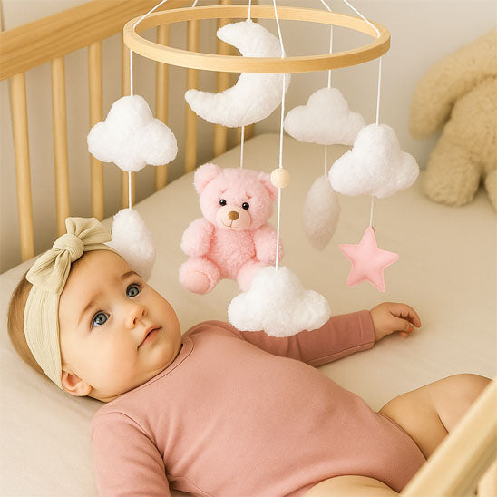 Mobile lit bébé ours rose Rosalia™ suspendu au-dessus d’un bébé éveillé dans un lit en bois.