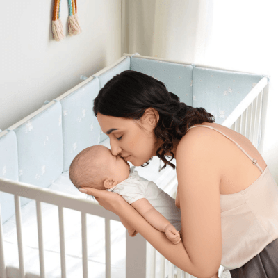 Maman tenant et embrassant son bébé endormi debout devant un berceau avec le Tour de Lit Bébé Bleu - Éléphandou™