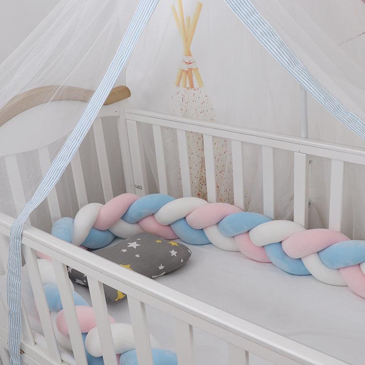 Tresse de lit bébé rose blanc bleu installé dans un berceau blanc avec une moustiquaire blanche et un petit oreiller gris avec des étoiles blanches et jaunes est posé dans le berceau