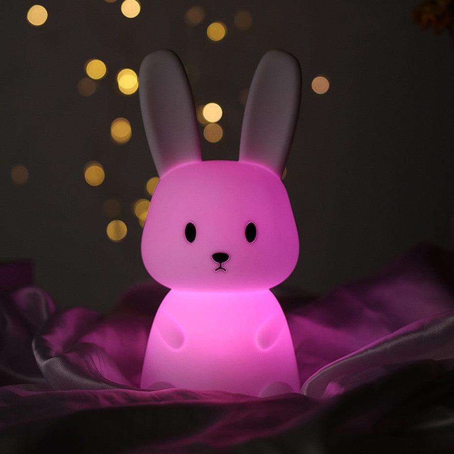Une VEILLEUSE BEBE MonsieurLapinou posée sur un lit allumée en couleur rose