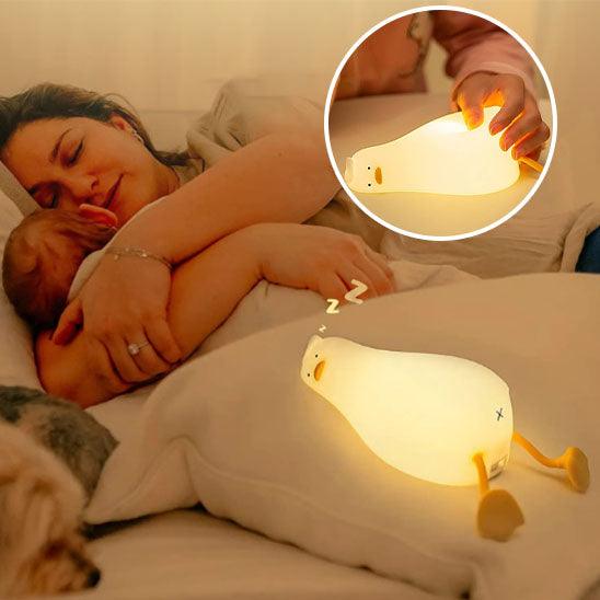 Une maman dort avec son bebe dans les bras et une VEILLEUSE BEBE CANARD - MonsieurCoinCoin™ est posée sur un coussin sur le lit
