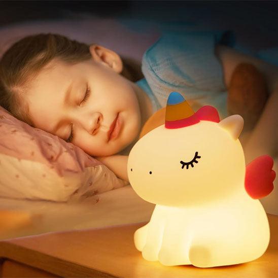Une petite fille dort avec une VEILLEUSE BEBE LICORNE - MissUnicorn™allumée sur sa table de nuit