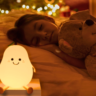 Une petite fille dort avec son ours en peluche dans les bras sur sa table de chevet est posée une VEILLEUSE BEBE POIRE