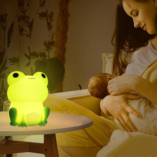 Maman allaitant son bébé près d’une veilleuse bébé grenouille verte posée sur une table