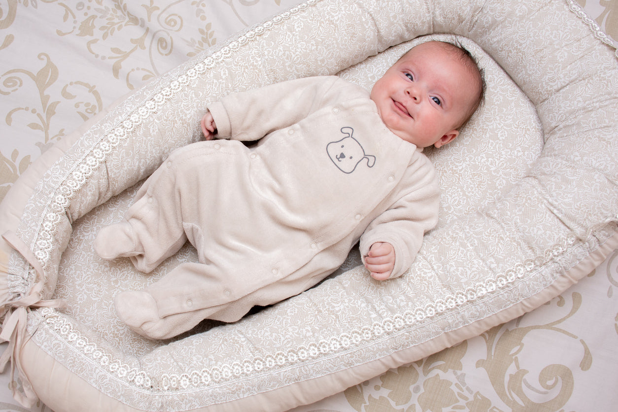 Bébé allongé et souriant dans un réducteur de lit cocon beige, ambiance douce et sécurisée