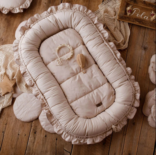 COCON BEBE CONFORT │ Nidamour™  beige présenté sur un parquet en bois clair autour de jouets d'enfant et de couverture de a même couleur