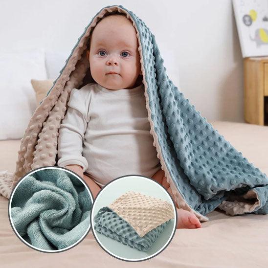 Un bébé assis au sol avec sur la tête la COUVERTURE BEBE REVERSIBLE -  DouceBulle™