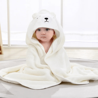 Un bébé assis au sol porte un Cape de Bain Bébé  - Douceur Câline™motif ours-blanc avec la capuche sur la tête