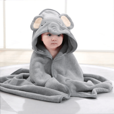 Un bebe assis au sol porte le Cape de Bain Bébé  - Douceur Câline™Grise motif éléphant avec la capuche sur la tête