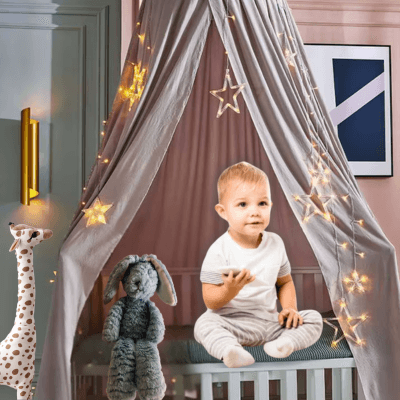 Bébé assis sous le Ciel de Lit Bébé Gris│ PierreDeLune™, entouré d’un voile protecteur et apaisant.