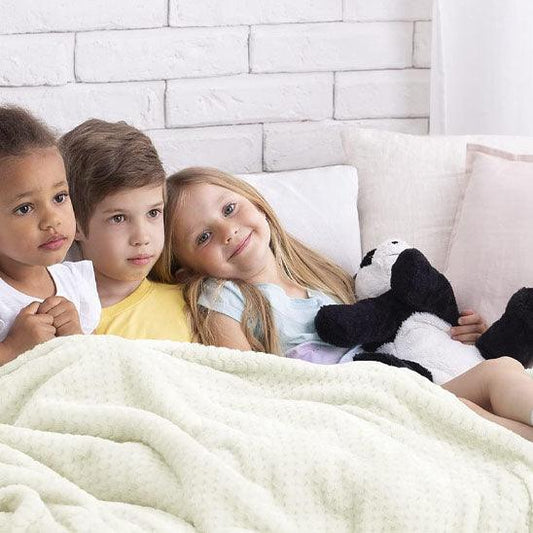 Trois enfant assis sur un canape blanc en cuir sont recouverts d'une Couverture Bébé en Minky Polaire - blanche  