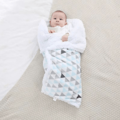 Un bébé allongé sur le dos emmailloté dans une couverture bébé Hiver chaudou bleue