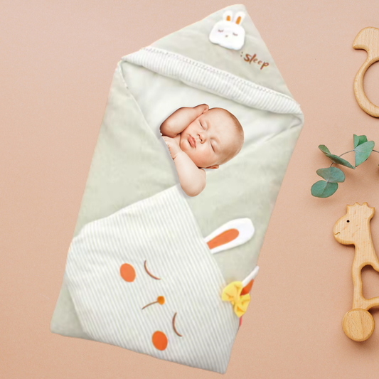 Bébé endormi paisiblement dans une couverture à capuche vert sauge décorée d’un lapin brodé et d’un nœud jaune.
