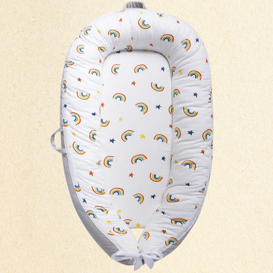 Nid_bebe portable_NaturaNid_motif_arc-en-ciel_multicolore_presente_vide_sur_fond_jaune_pale_cocon_ergonomique_pour_nouveau-ne