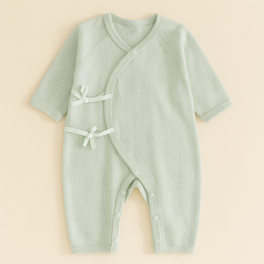 Pyjama bebe vert sauge mi-saison en coton respirant, avec coutures plates et nœuds latéraux, présenté sur fond uni pour un rendu élégant.
