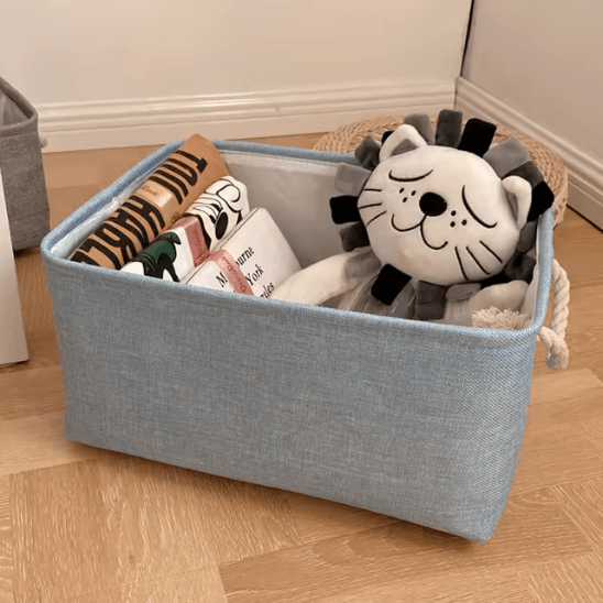 Panier de Rangement Pour Bébé bleu posée au sol avec des Tshirts et un ourson dedans