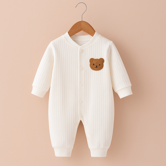 Pyjama bebe blanc en coton sans pied suspendu sur cintre en bois, avec petit motif ours, présenté sur fond rosé poudré doux pour un rendu élégant et chaleureux.