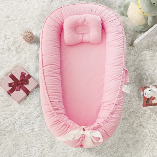 Réducteur de lit bébé rose avec fronces et nœud blanc, posé sur un tapis moelleux - design cocon confortable avec coussin ergonomique.