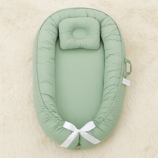 Reducteur de lit bebe vert sauge BambouNid™ vu de dessus sur un tapis moelleux, ambiance douce et naturelle.