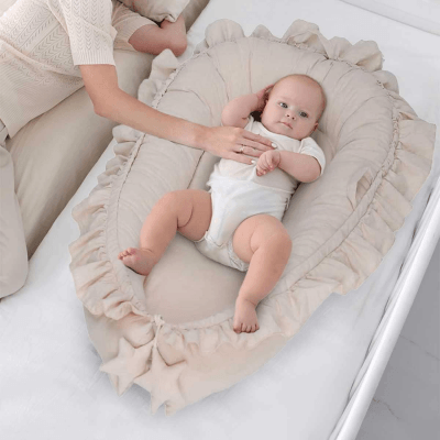 Bébé confortablement  installé dans le REDUCTEUR DE LIT BEIGE - Rêve de Lin™ . La main de sa maman posée sur son ventre pour lui faire un calin 
