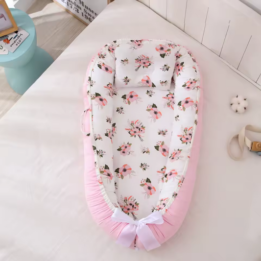 Réducteur de lit bebe fleuri rose et blanc avec détails réalistes du coussin, des bords rembourrés et du ruban ajustable, sur fond pastel.
