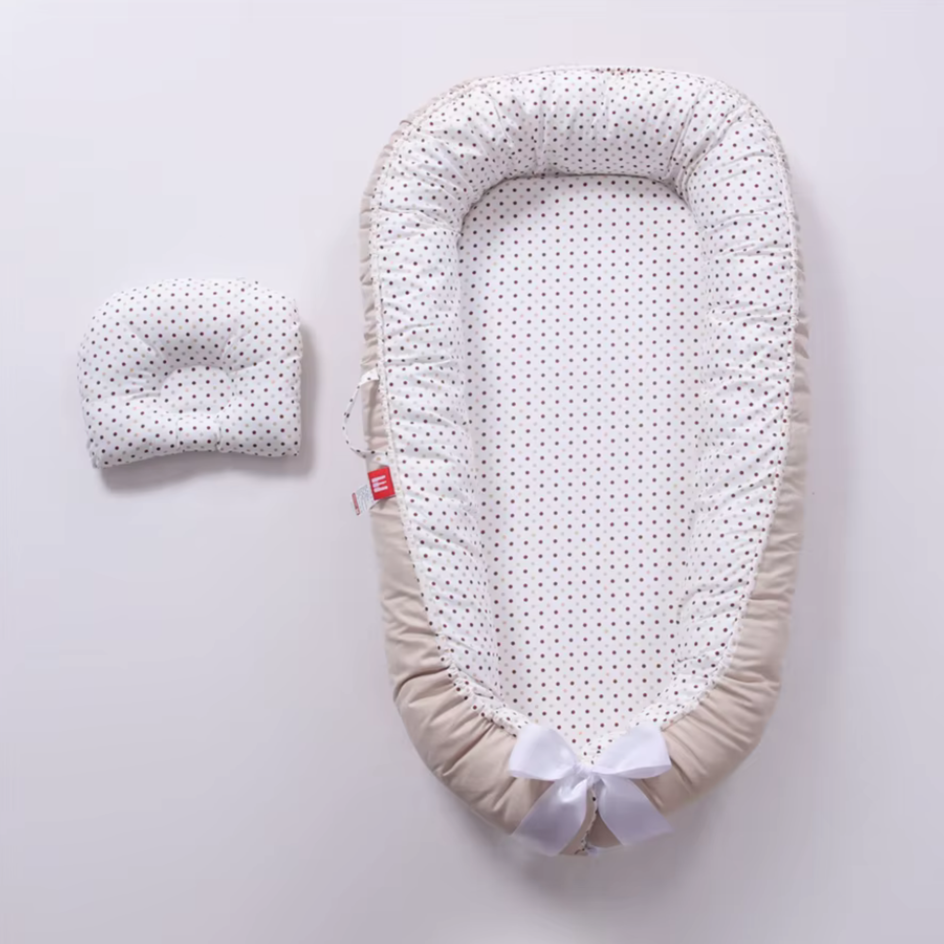 Réducteur de lit bebe beige avec coussin assorti à pois, présenté à plat vu de dessus.