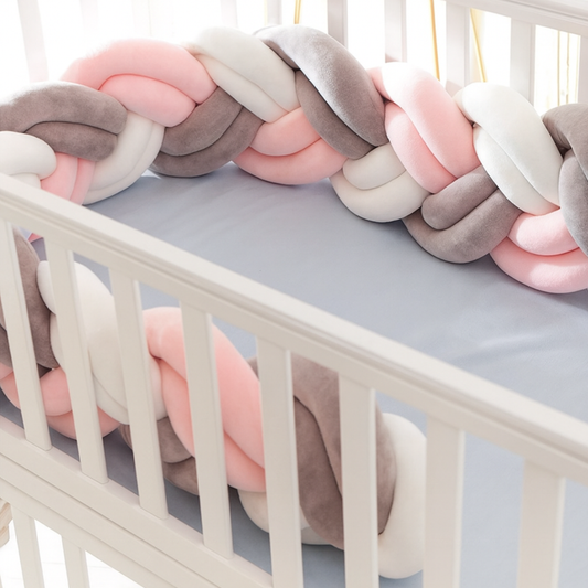Tresse de lit bébé 6 brins rose, blanc et gris installée dans un berceau blanc, créant un cocon sécurisant et doux pour le sommeil de bébé.