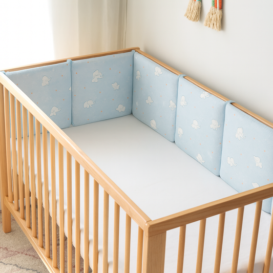 Berceau en bois clair avec tour de lit bleu à motifs d’éléphants blancs, installé dans une chambre lumineuse au style doux et épuré.