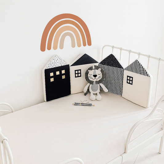 Décoration de chambre bébé avec le tour de lit modulable en forme de maisonnettes noires et blanches, peluche lion gris au centre arc en ciel au mur