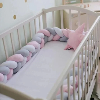 Tresse de lit bébé rose gris et blanc installée dans un berceau en bois, créant une protection douce et sécurisée dans une chambre scandinave.