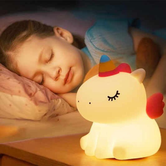 Une petite fille dort avec une VEILLEUSE BEBE LICORNE - MissUnicorn™allumée sur sa table de nuit