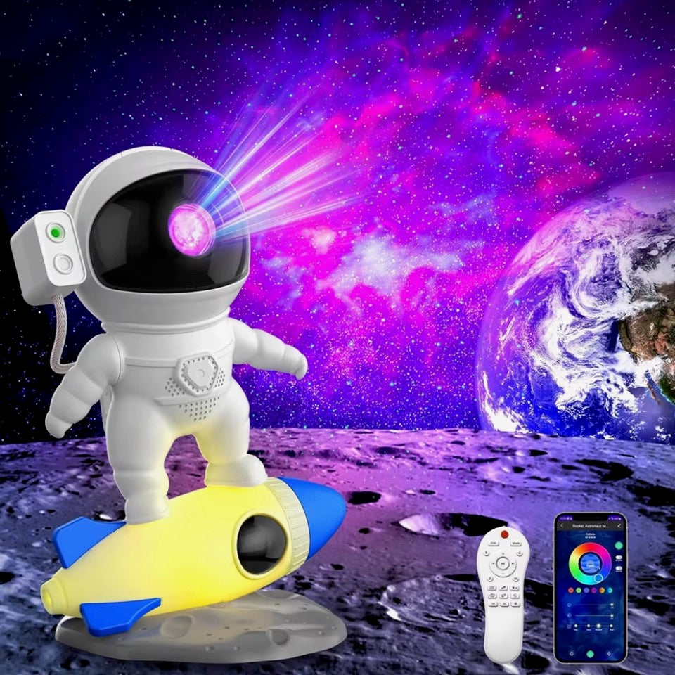 Veilleuse astronaute à projection sur une fusée jaune et bleue, avec fond galactique violet et Terre et télécommande visibles.