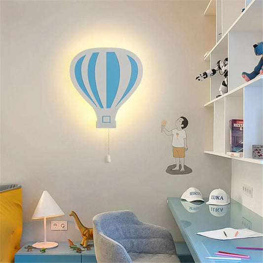 Une Veilleuse bébé Murale Marco Polo bleue sur un mur dans une chambre au dessus une petite table de chevet bleue à droite une biliothèque blanche un bureau bleu et un fauteuil gris