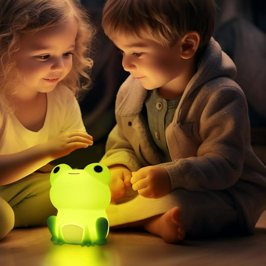 Deux enfants jouent avec une veilleuse grenouille bébé lumineuse posée au sol