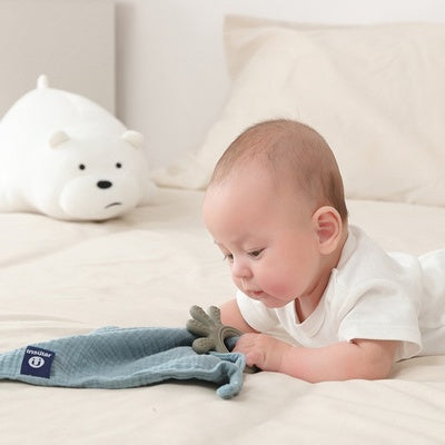 Bébé sur le ventre jouant avec un doudou avec anneau de dentition bébé bleu vert 