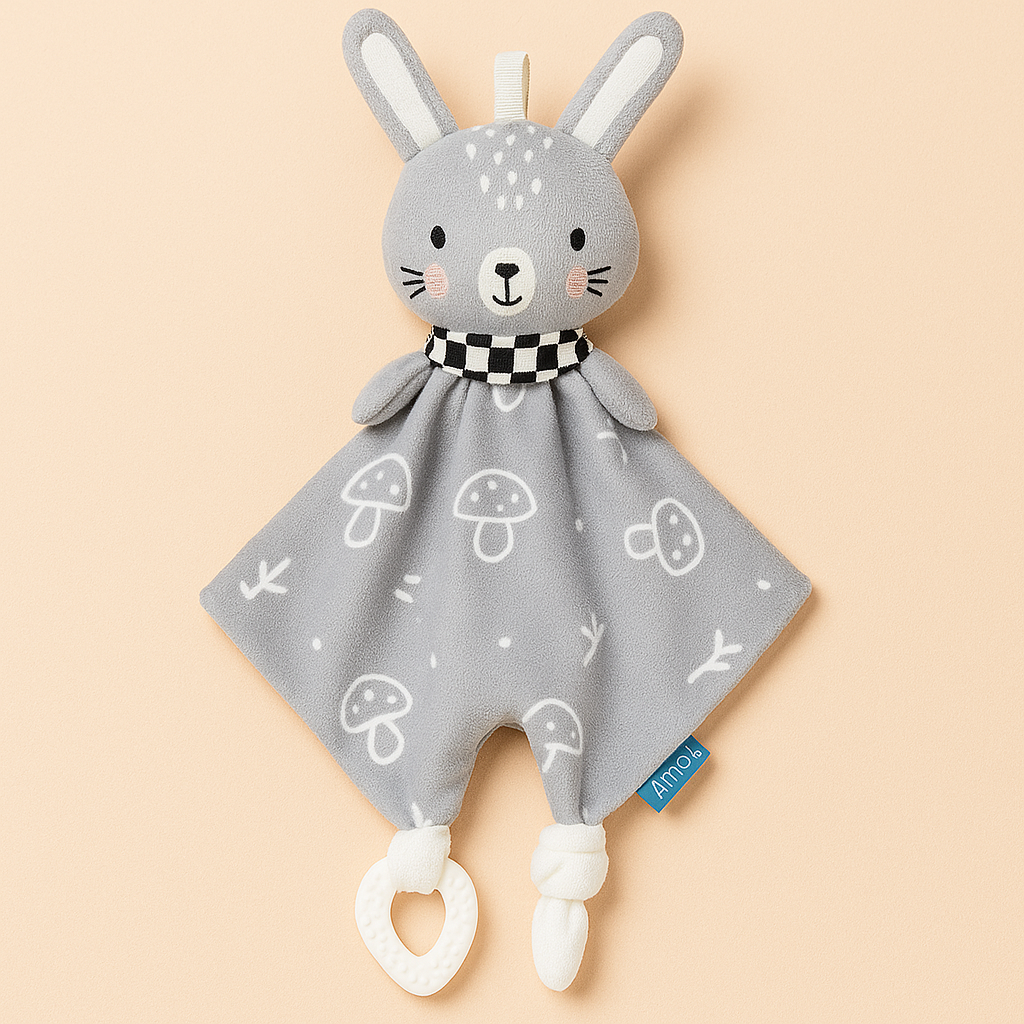 Doudou bébé Toloman modèle lapin, présenté sur un fond beige rosé, avec tissu gris à motifs champignons et anneau de dentition en silicone