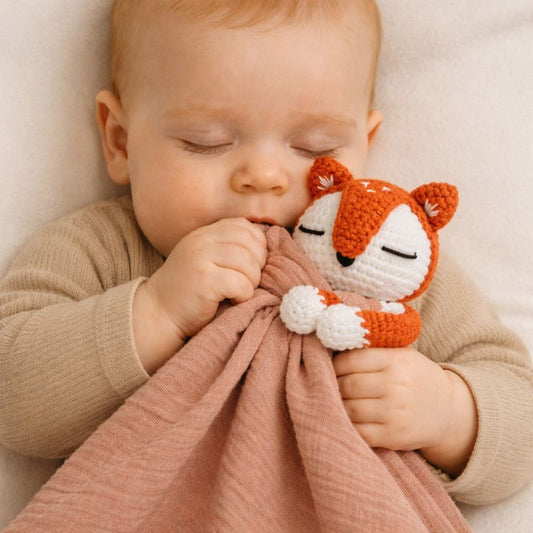 Bébé endormi tenant un doudou pour bébé au crochet renard et mâchouillant le lange rose
