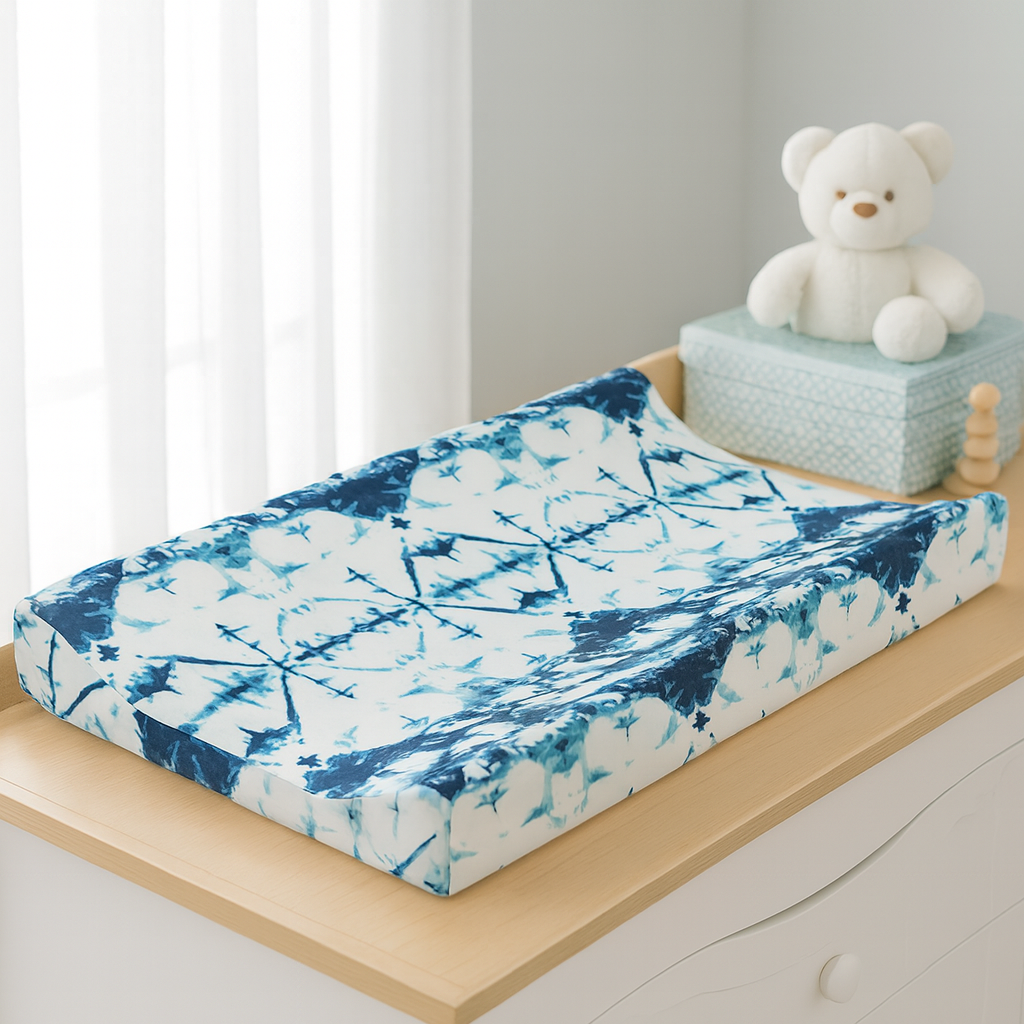 Housse matelas à langer imperméable LeafyCare™ motif bleu tie-dye, présentée sur une table à langer dans une chambre bébé lumineuse.