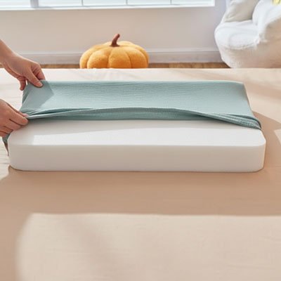 Parent installant une housse pour matelas à langer verte en coton sur un matelas en mousse.